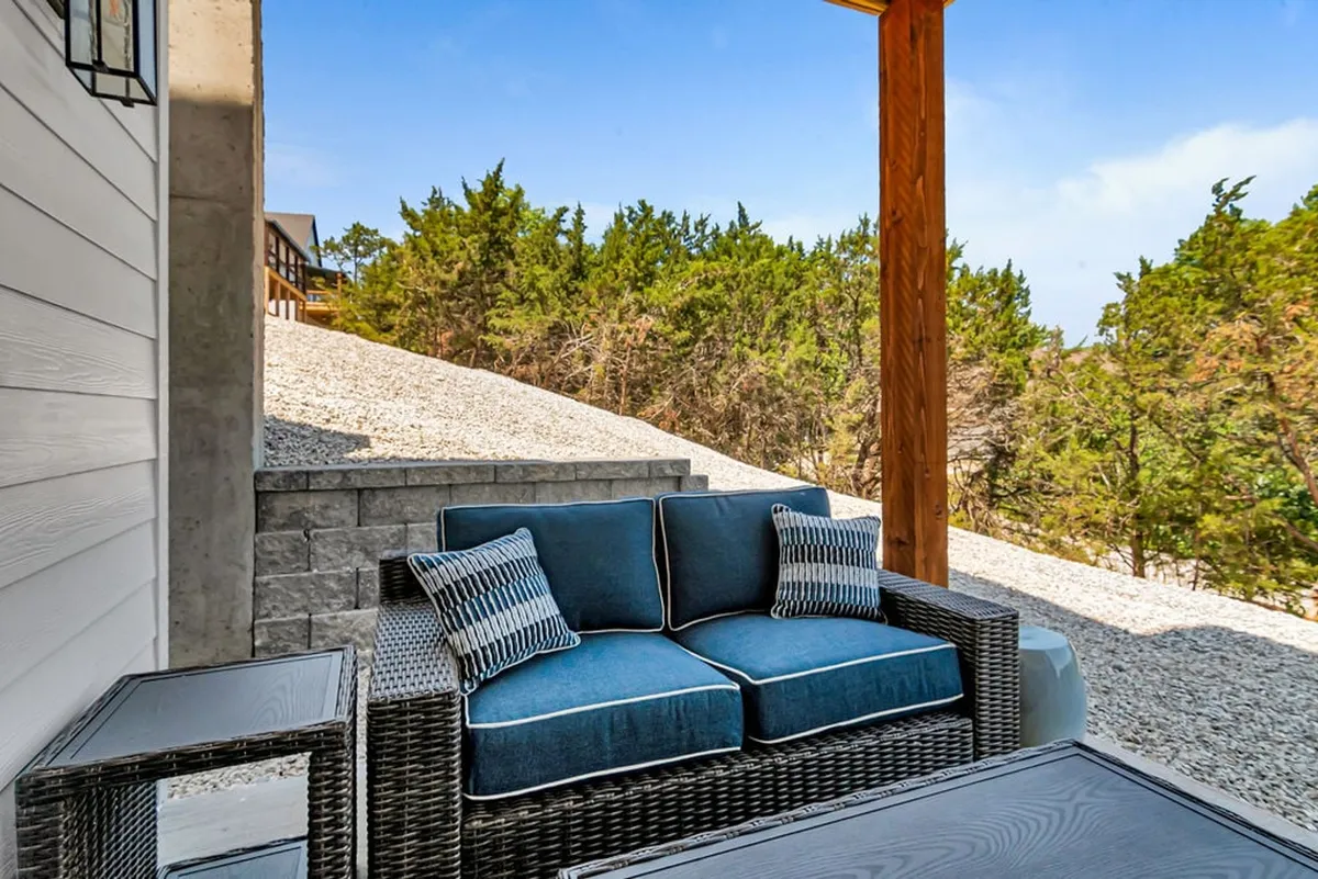 This exterior shot displays a peaceful outdoor seating area surrounded by lush greenery and a rustic stone wall, perfect for relaxing with a book, entertaining guests, or enjoying morning coffee. It captures a sense of tranquility and connection to nature.