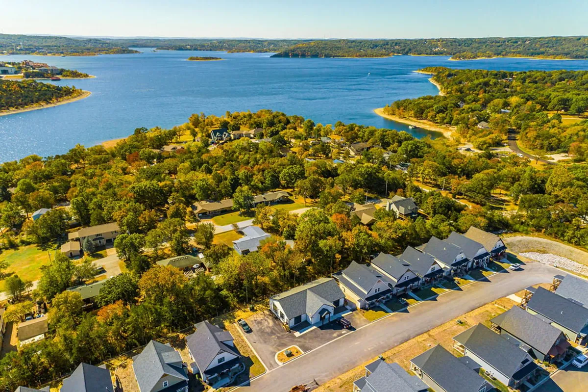 A sweeping view of Table Rock Lake with surrounding greenery, rows of nearby houses, and tranquil water stretching toward the horizon. The scene suggests boating, fishing, hiking, and a wealth of outdoor activities available just beyond the property.