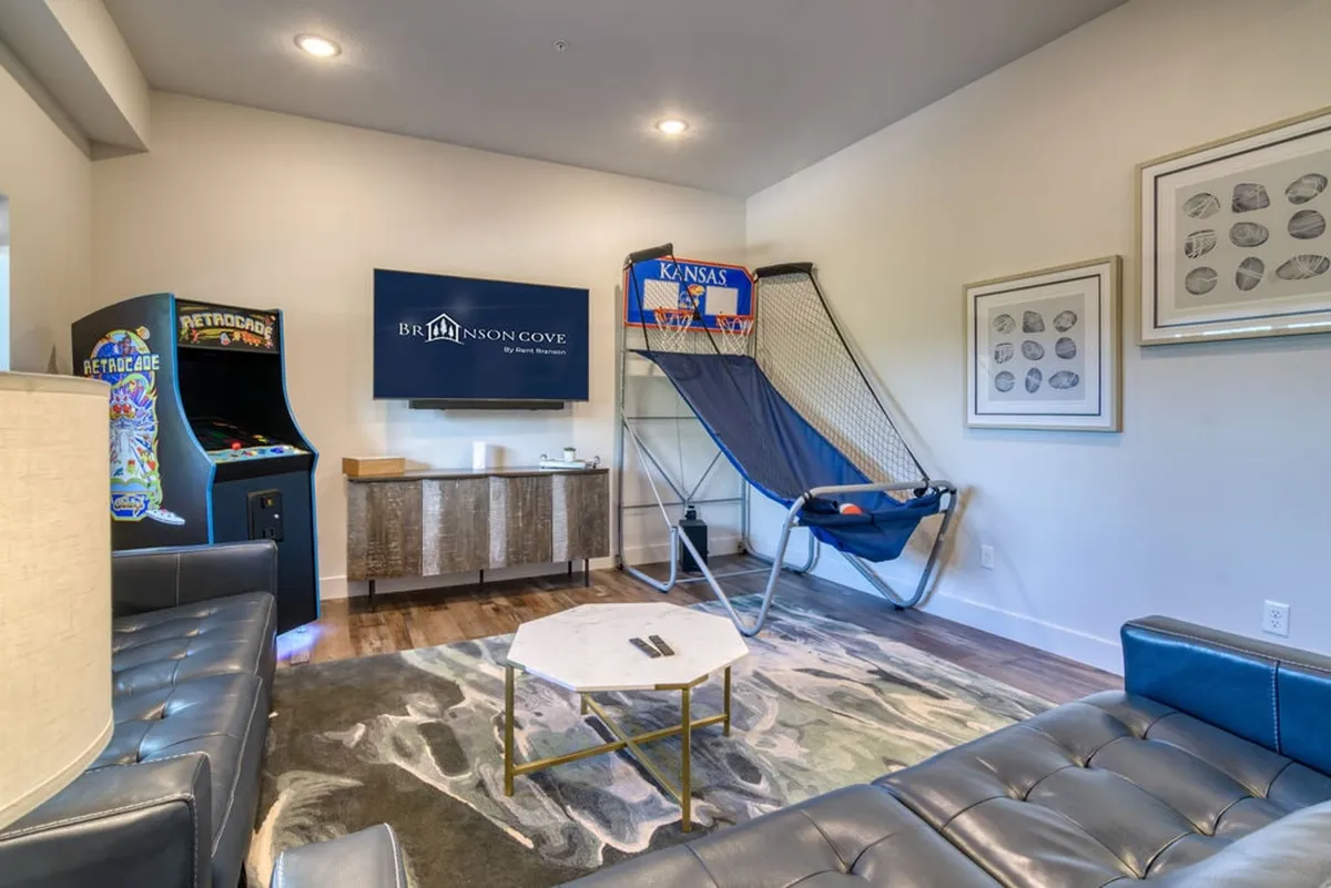 This image shows an interior recreation space with an arcade game machine, basketball hoop, TV with branding, and a coffee table. The area is designed for fun and friendly competition, ideal for game nights with friends or family.