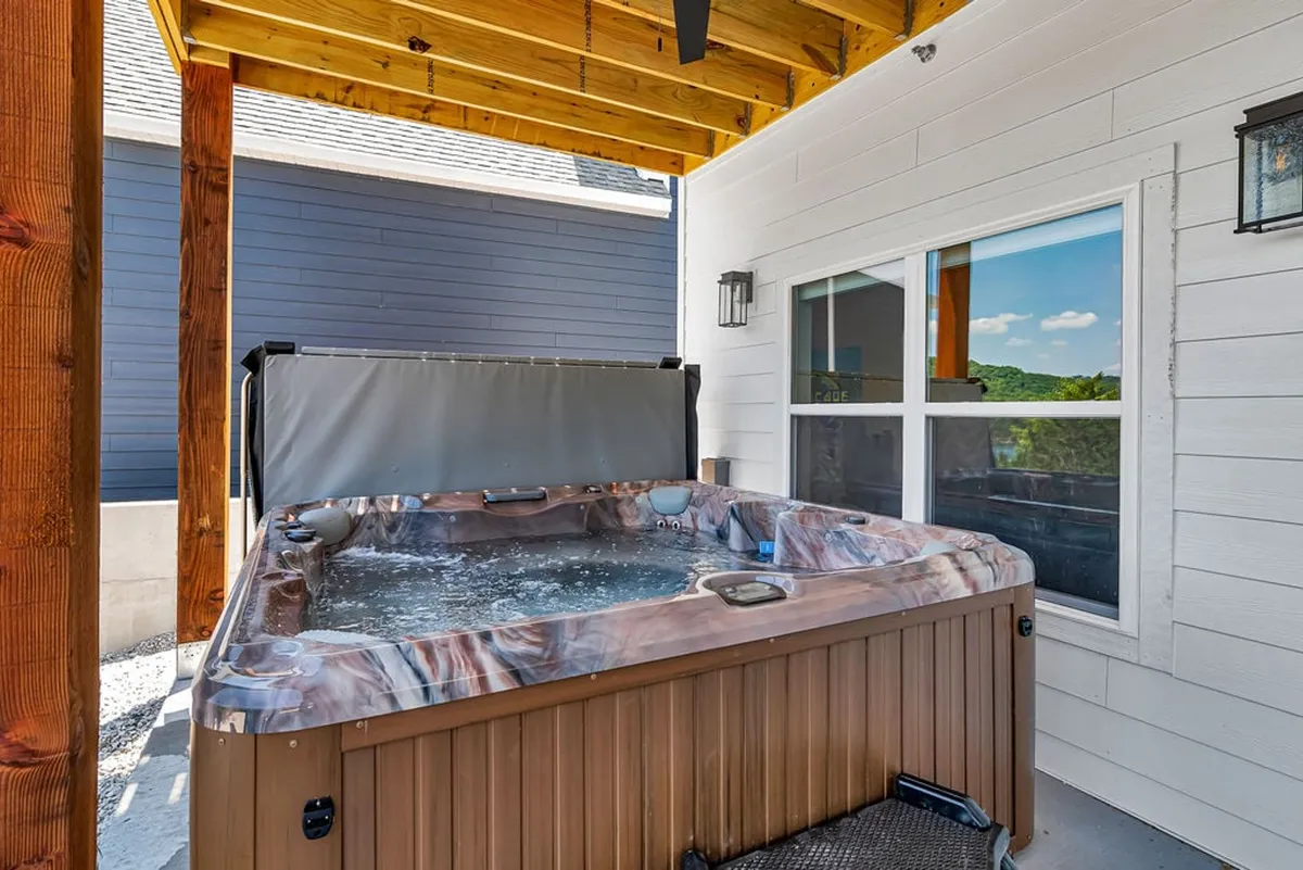 An inviting exterior patio features a private hot tub, sturdy wooden beams, and a tranquil outdoor setting. The view hints at sunset or twilight, with the water reflecting soft light, perfect for relaxation or socializing.