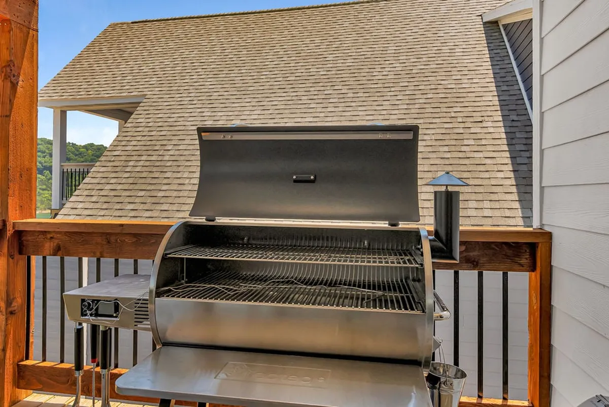 A state-of-the-art grill stands on a covered deck, bordered by a sturdy railing and a roof structure offering shade. The setup is ideal for barbecuing and socializing, with space to linger and enjoy the lake breeze and views.
