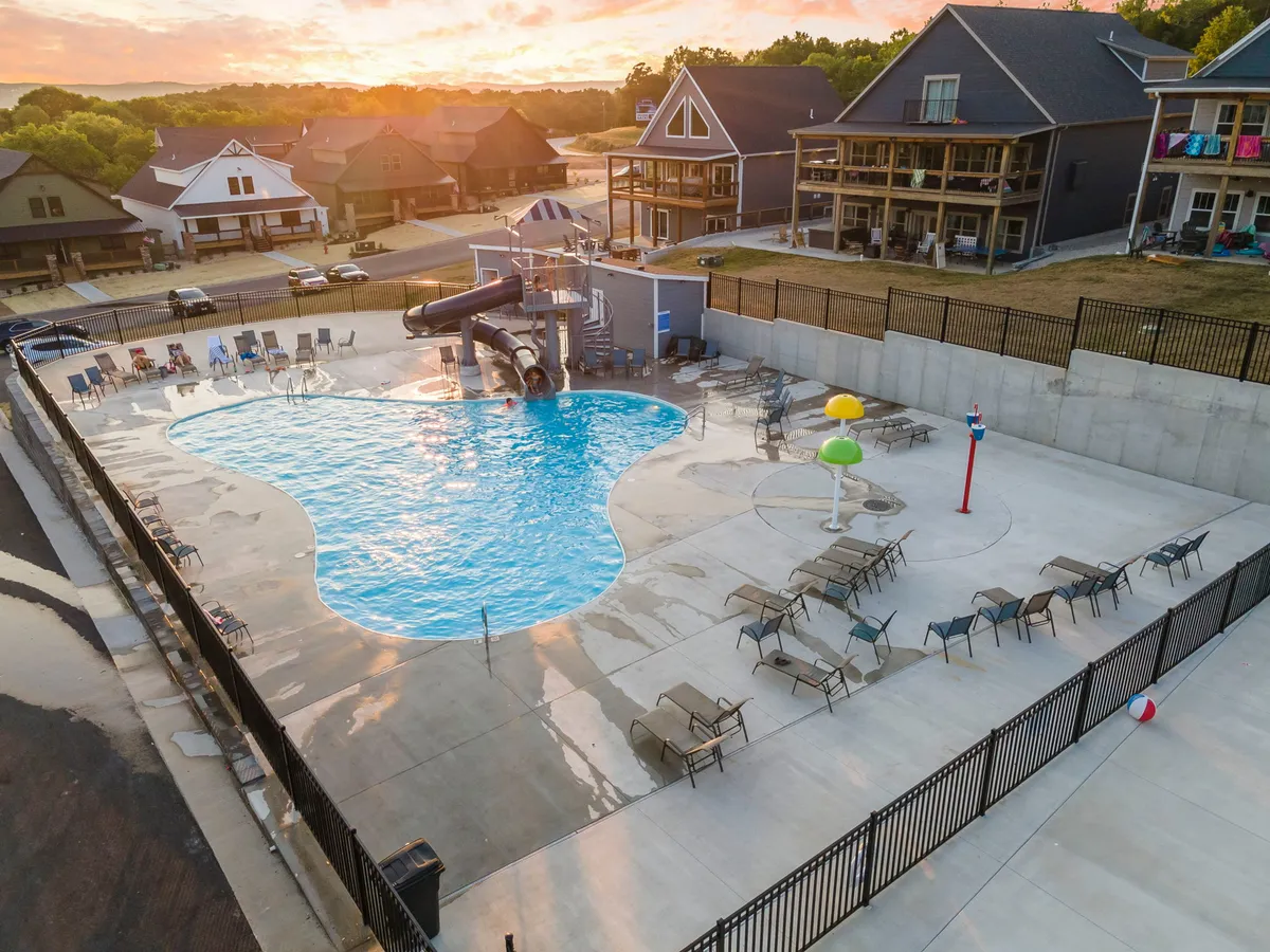 An inviting outdoor swimming pool area with an exciting water slide, lounge chairs, and a play area with water features. Families and children are enjoying the pool, highlighting a lively, resort-style amenity perfect for group gatherings and fun in the sun.