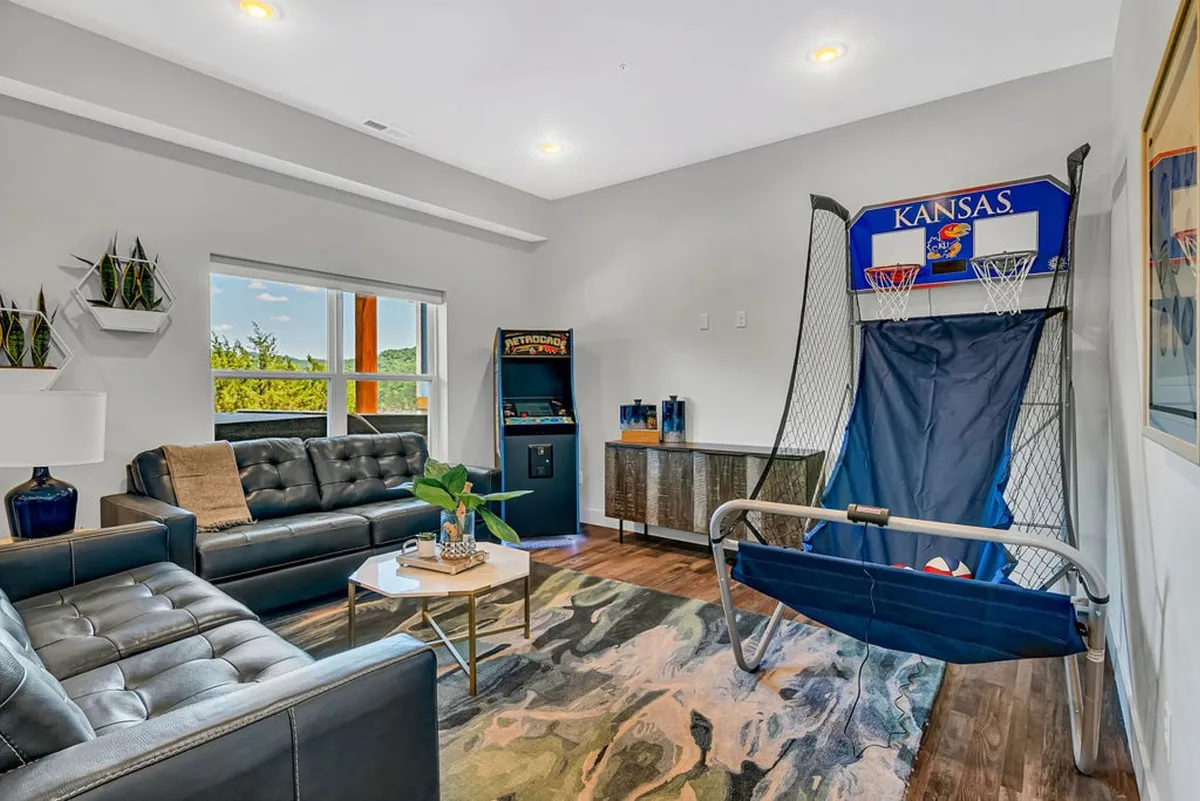 A fun-filled interior featuring a sofa, basketball game, and arcade machine. The coffee table and rug add comfort, making it ideal for both hanging out and active play. The area is welcoming for all ages, fostering relaxation and excitement.