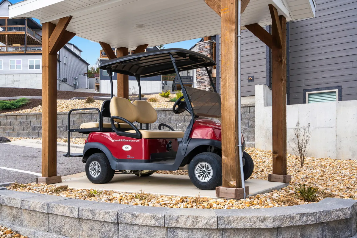 A stylish golf cart is parked near a wooden structure and neatly landscaped grounds, inviting guests to explore the surrounding property or venture to nearby attractions in comfort and style.