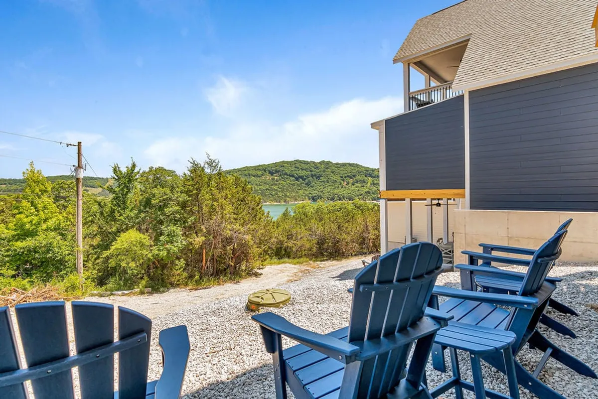 This image features blue Adirondack chairs circling a fire pit on a gravel area, with a serene lake view and trees in the background. The setting is perfect for gathering, socializing, and enjoying the outdoors, particularly at sunset or under the stars.