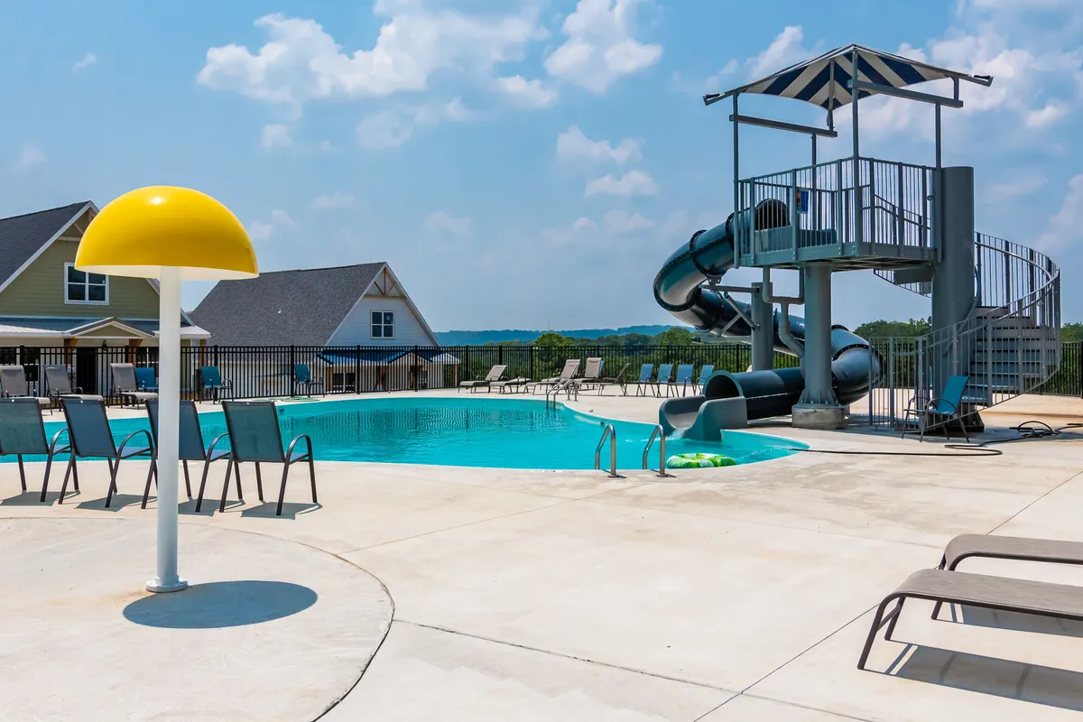 A vibrant outdoor pool scene featuring a sparkling swimming pool with a water slide, shaded by a bright yellow umbrella. Guests are swimming, sunbathing, and dashing down the slide, while the overall atmosphere is filled with energy and summer fun.
