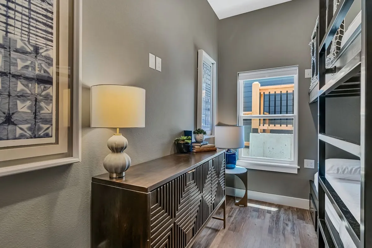 A cozy bunkroom scene with a bunk bed, bedside lamp, window, and playful artwork. The space is designed for comfort and togetherness, providing a cheerful spot for children and families to read, play, or simply relax.