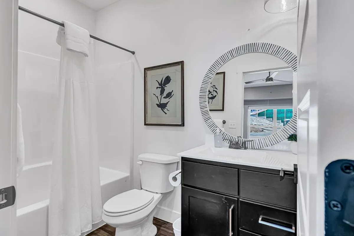 A modern bathroom sanctuary with a circular mirror, sleek black vanity, and framed botanical prints. The inviting, spa-like setting is designed for moments of self-care and relaxation, echoing the comfort of a premium retreat.