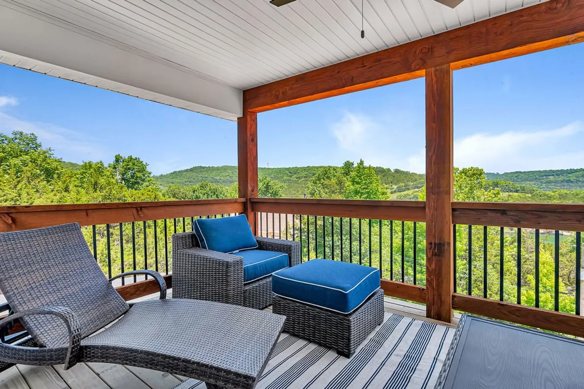 An exterior deck with a reclining chair featuring blue cushions and a wooden railing overlooks a tranquil mountain view. The setting suggests serenity, with ample room for both people and small pets to enjoy the outdoors together.